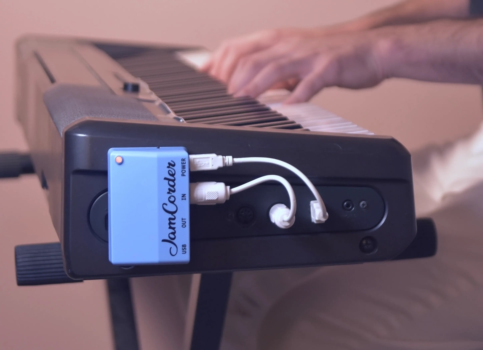 A JamCorder device affixed to the side of a digital piano, with MIDI cables attached